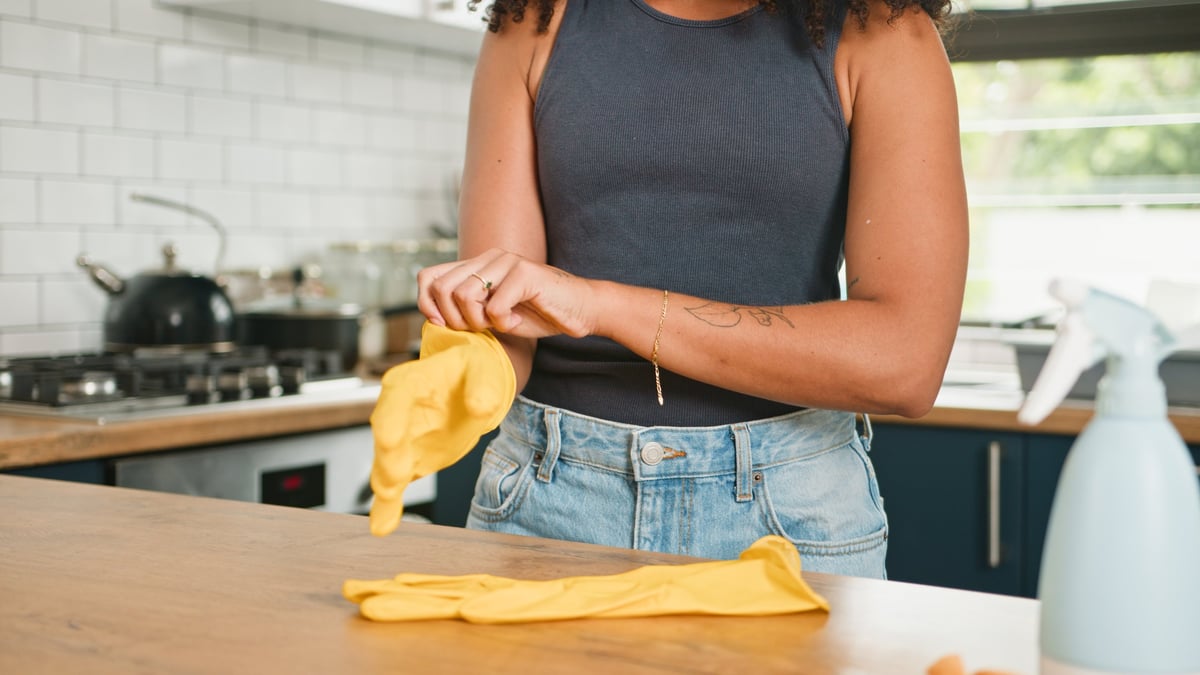 Person pulling on cleaning gloves at a bright modern kitchen counter